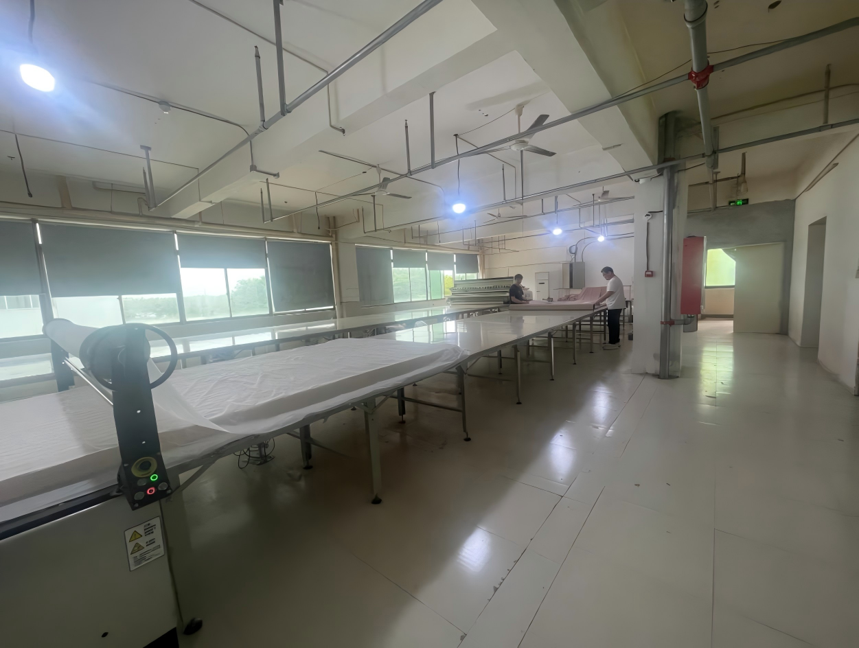 Cutting area with long tables, a fabric spreading machine and two workers at the far end of the room