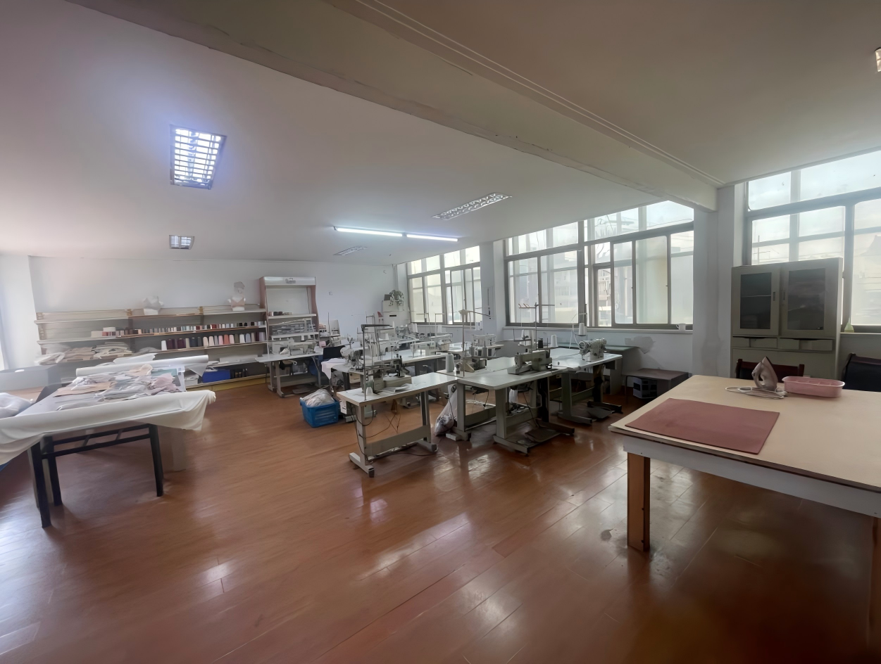 Sampling room with sewing machines, shelves of thread cones, mannequin busts and a pressing table